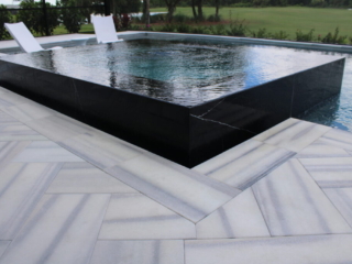 Raised dark-tiled spa with a spillway above a light patterned pool deck