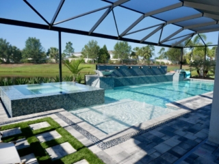 Screened pool and raised spa with a stone water-feature wall and patterned paver deck
