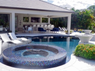 Round tiled spa beside a swimming pool, lounge chairs and a covered outdoor bar